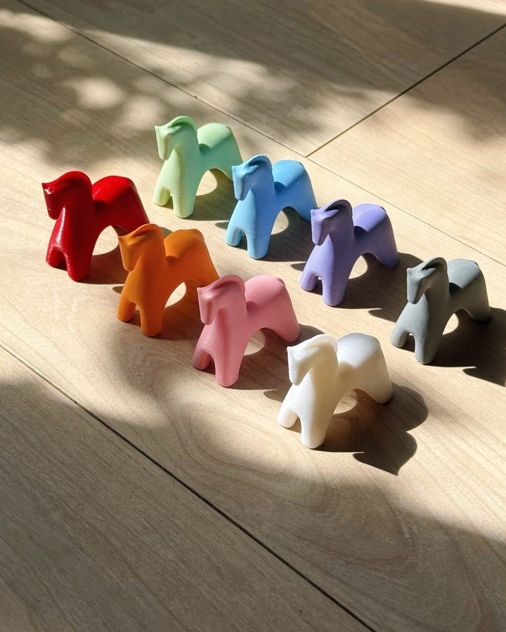 A row of Asa Studio horse charms in every colour, in afternoon sunlight on a wooden floor