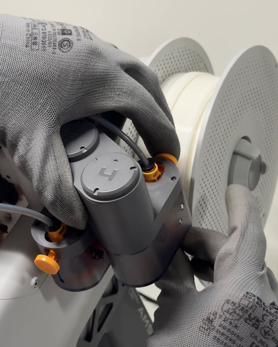 Gloved hands loading a spool of filament into the printer in the Asa Studio workshop
