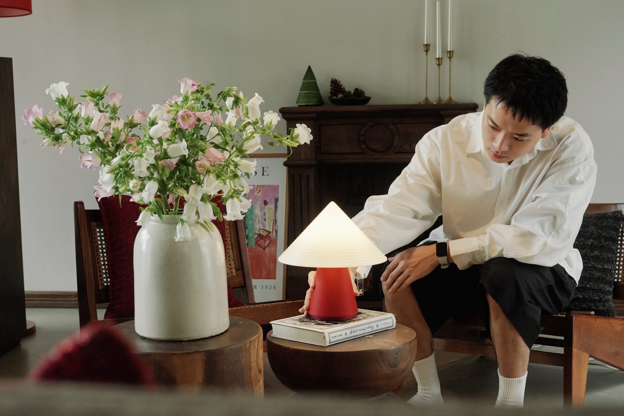Một người đang chỉnh đèn NOLA đỏ trên bàn trà, giữa không gian phòng khách ấm cúng